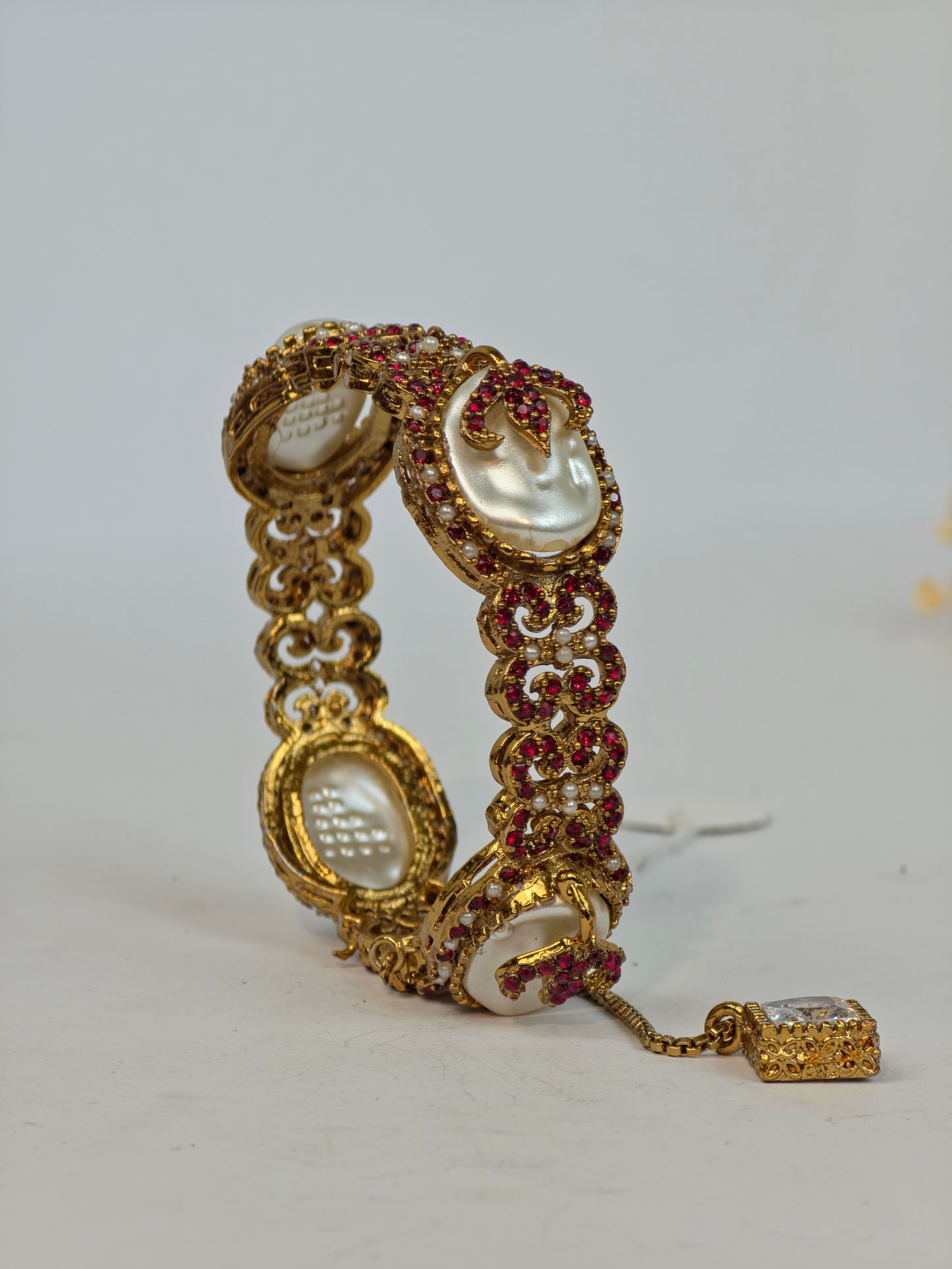 Gold bracelet with pearls and red stones on a white background