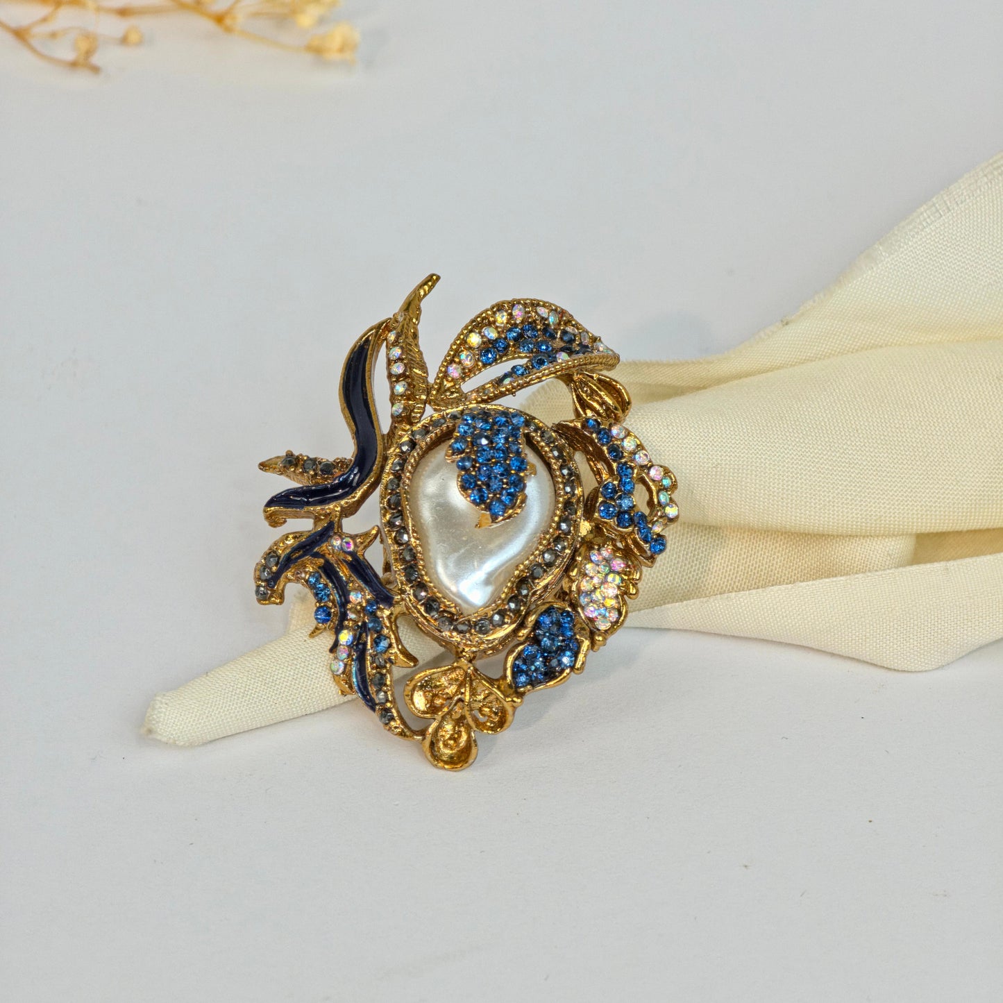 Decorative napkin ring with blue and gold accents on a white napkin against a light gray background.