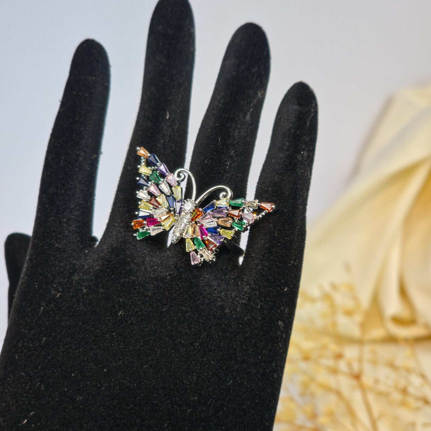 Multicolored brooch on a black hand with a blurred floral background