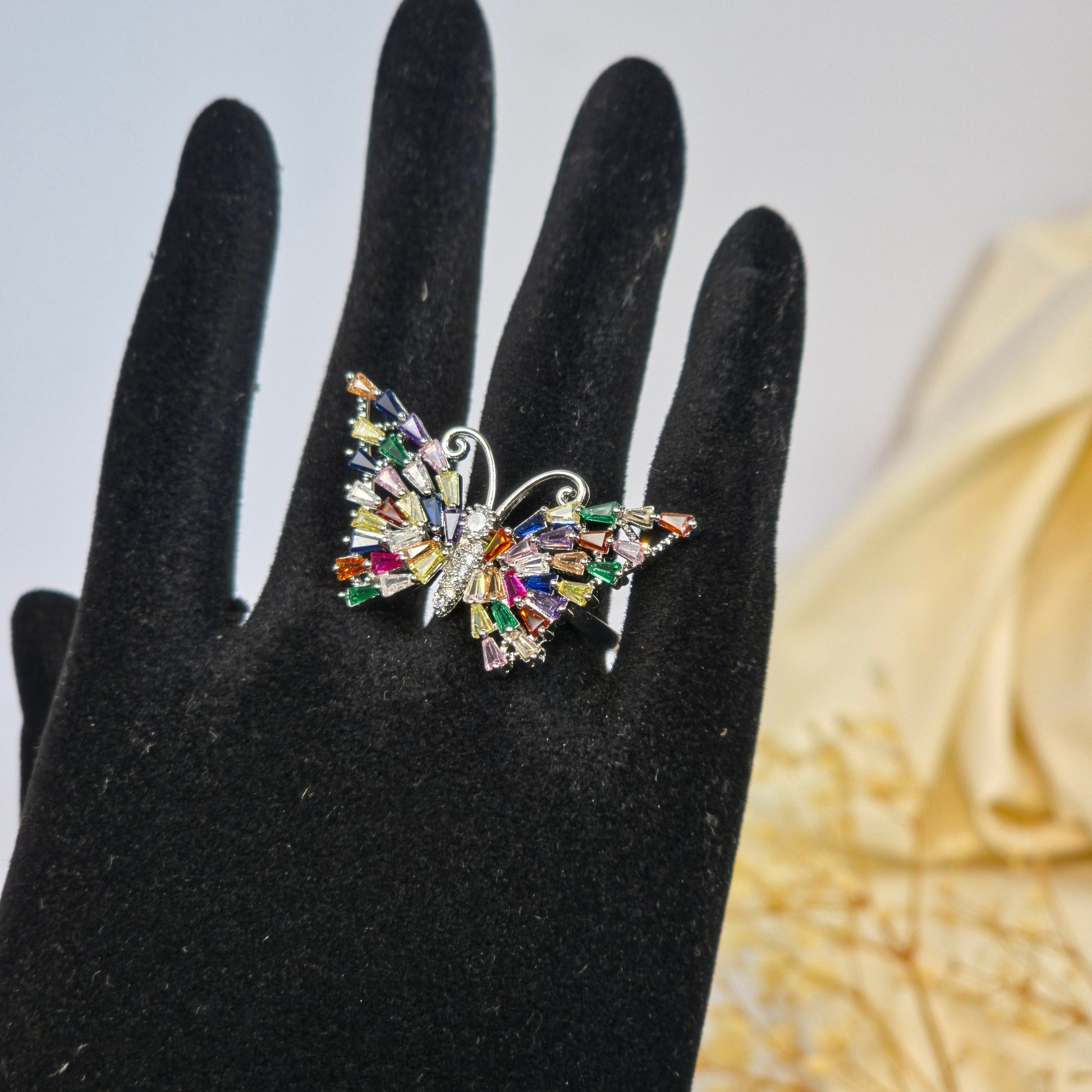 Multicolored brooch on a black hand with a blurred floral background