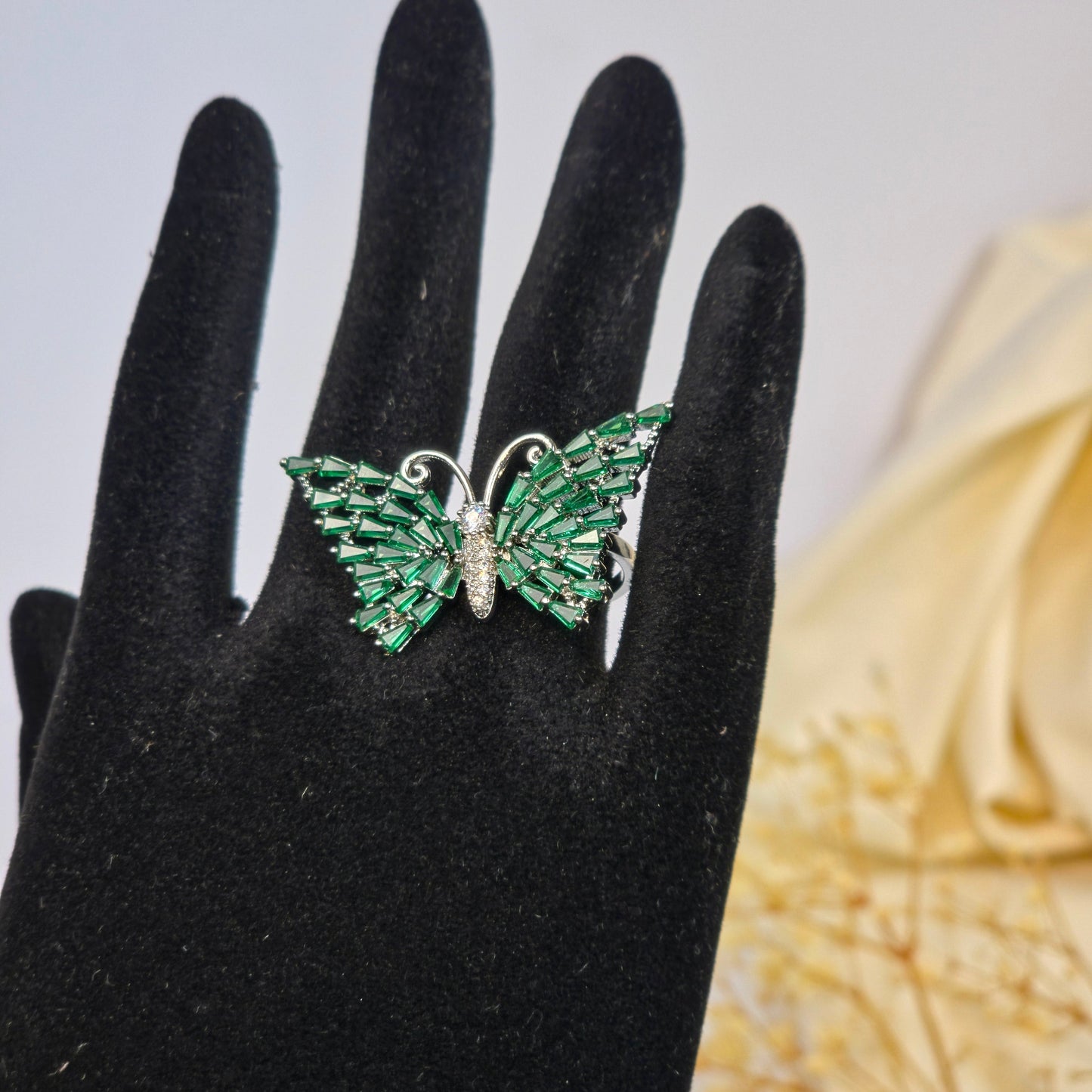 Green gemstone ring on a black-gloved hand with a blurred decorative background