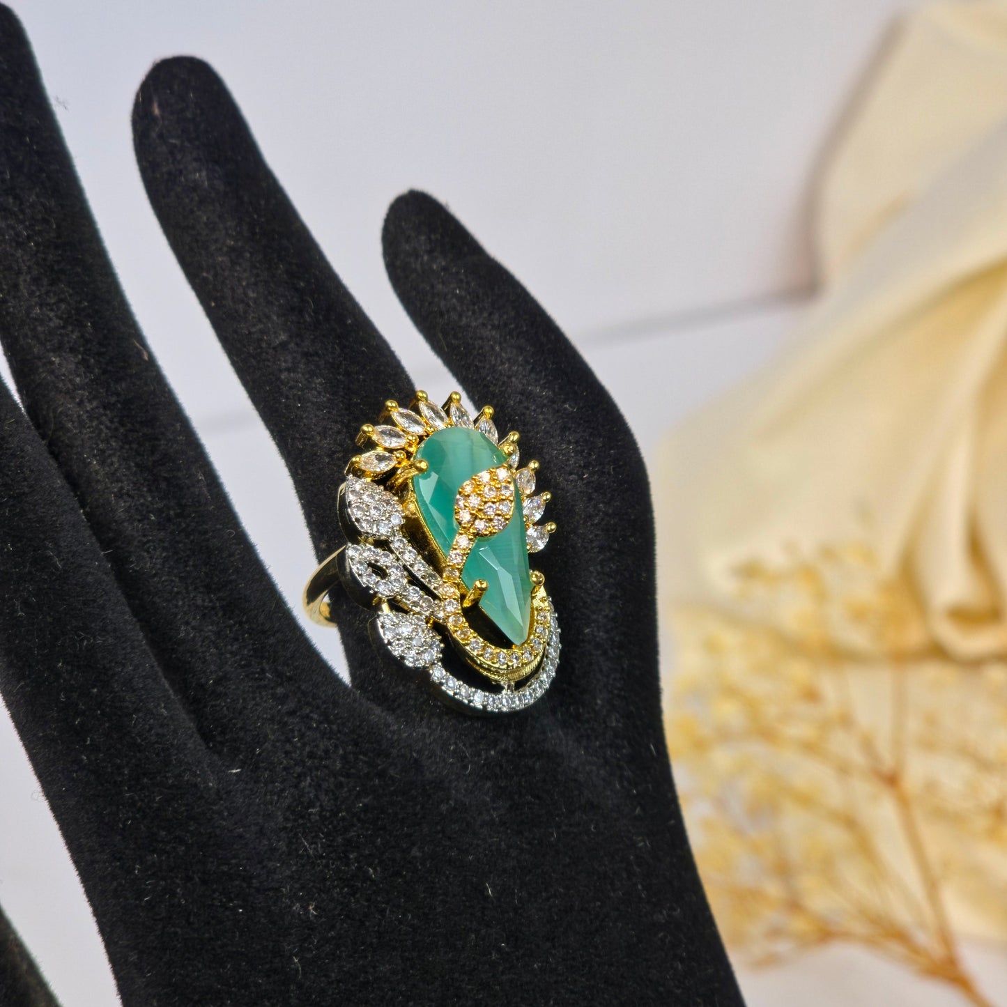 Green gemstone ring with gold accents on a black glove