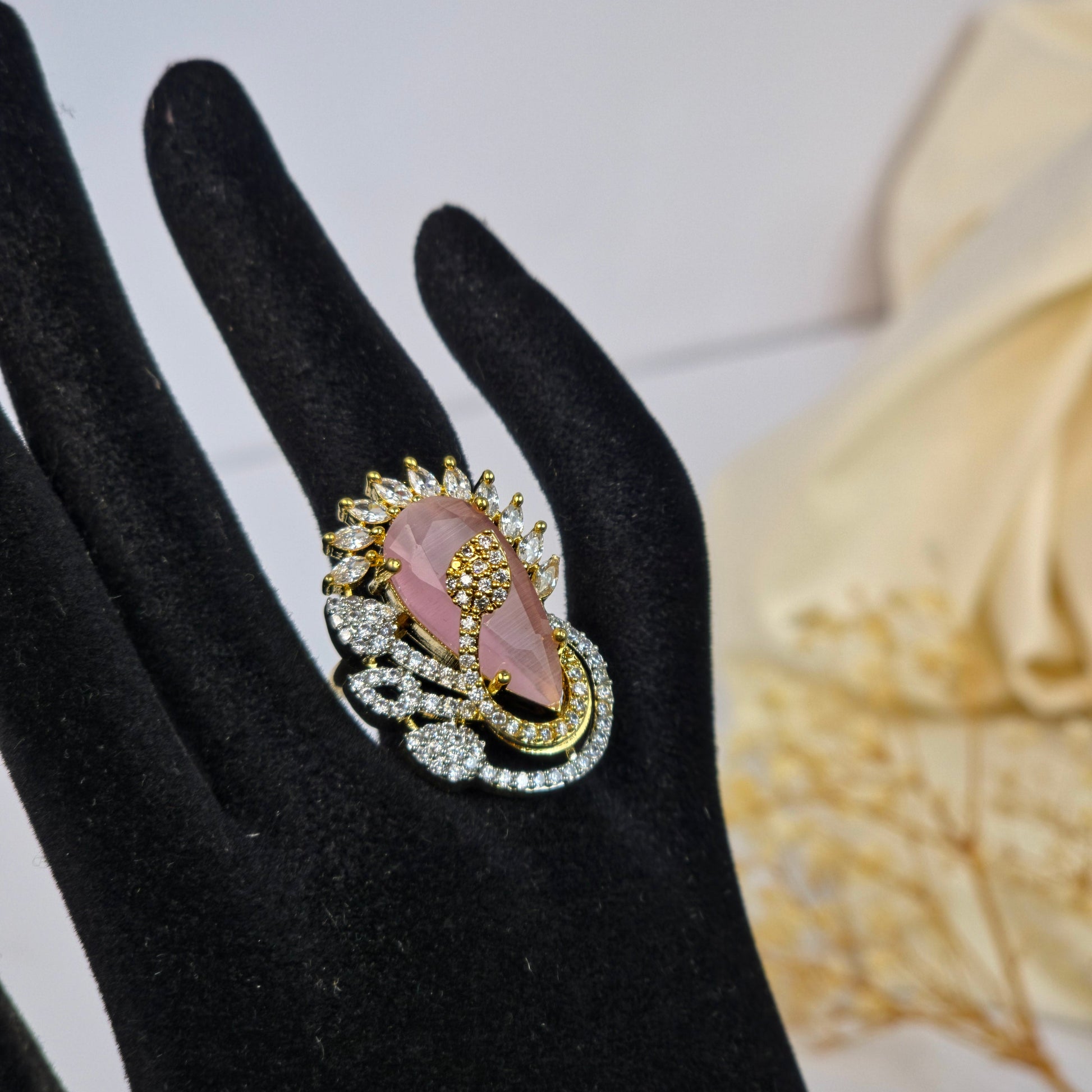 Decorative ring with pink gemstone and gold accents on a black hand model