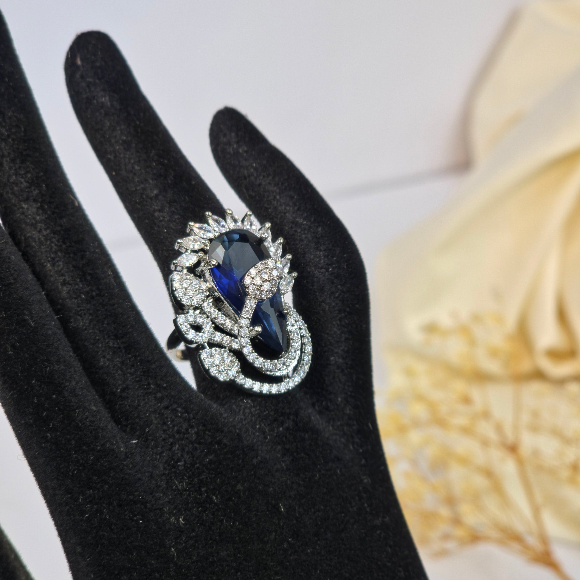Jewelry ring with blue gemstone and diamond-like stones on a black glove