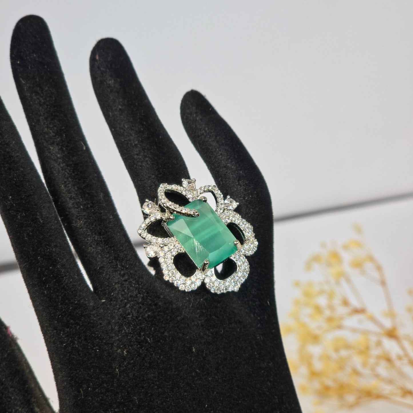 Ring with a green gemstone and diamond-like accents on a black glove.