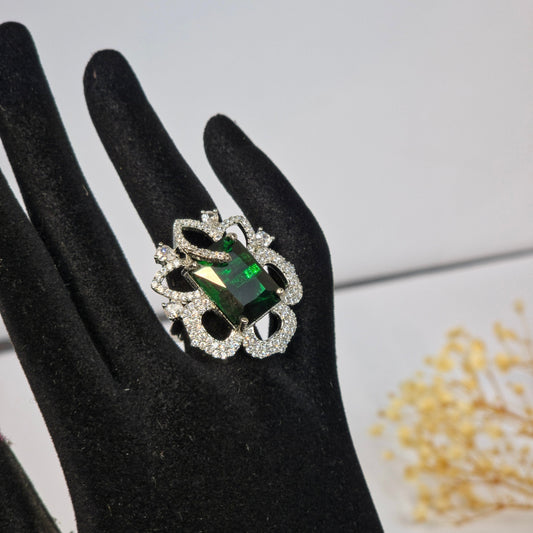 Ring with a green gemstone on a black glove against a light gray background