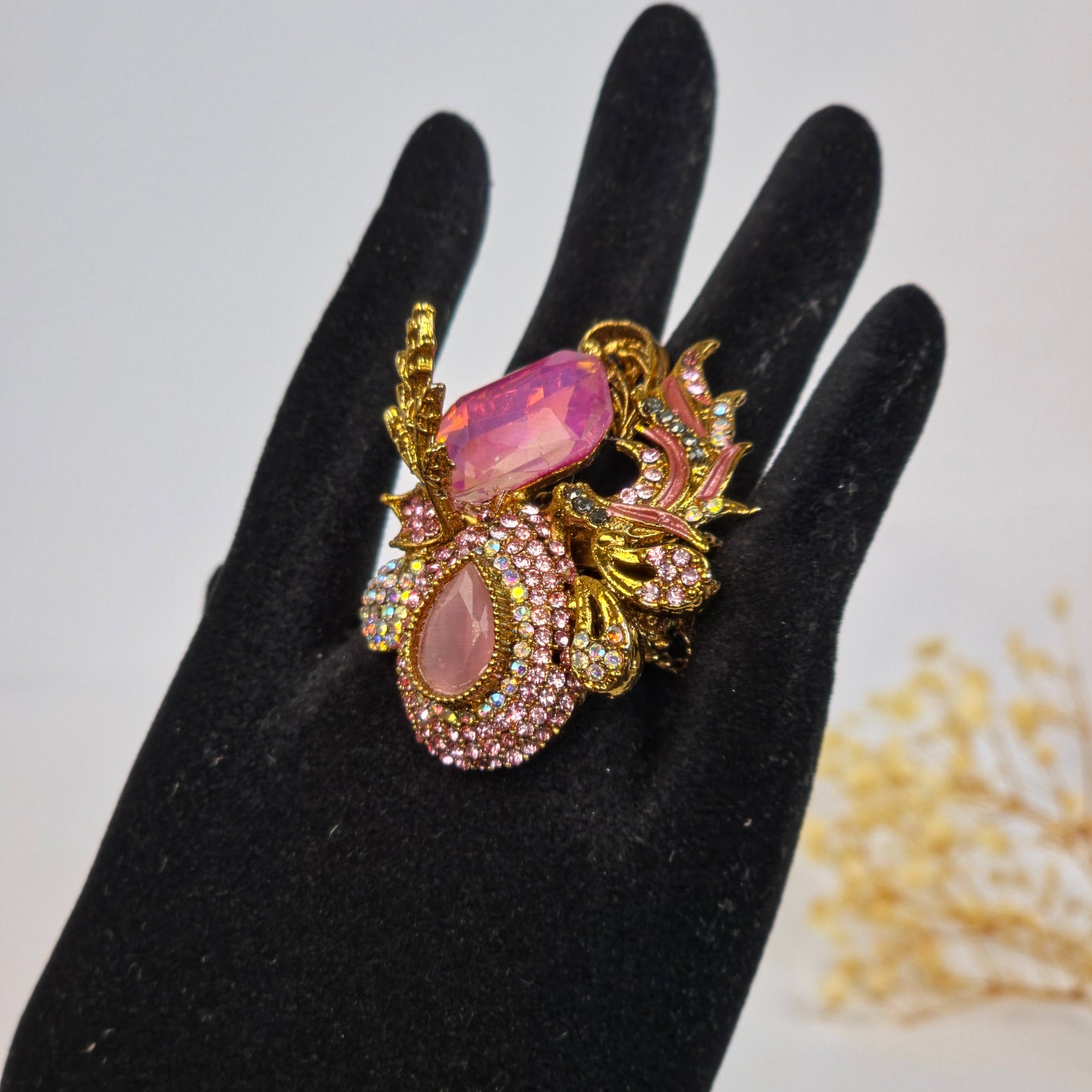 Decorative ring with pink gemstones on a black glove against a neutral background