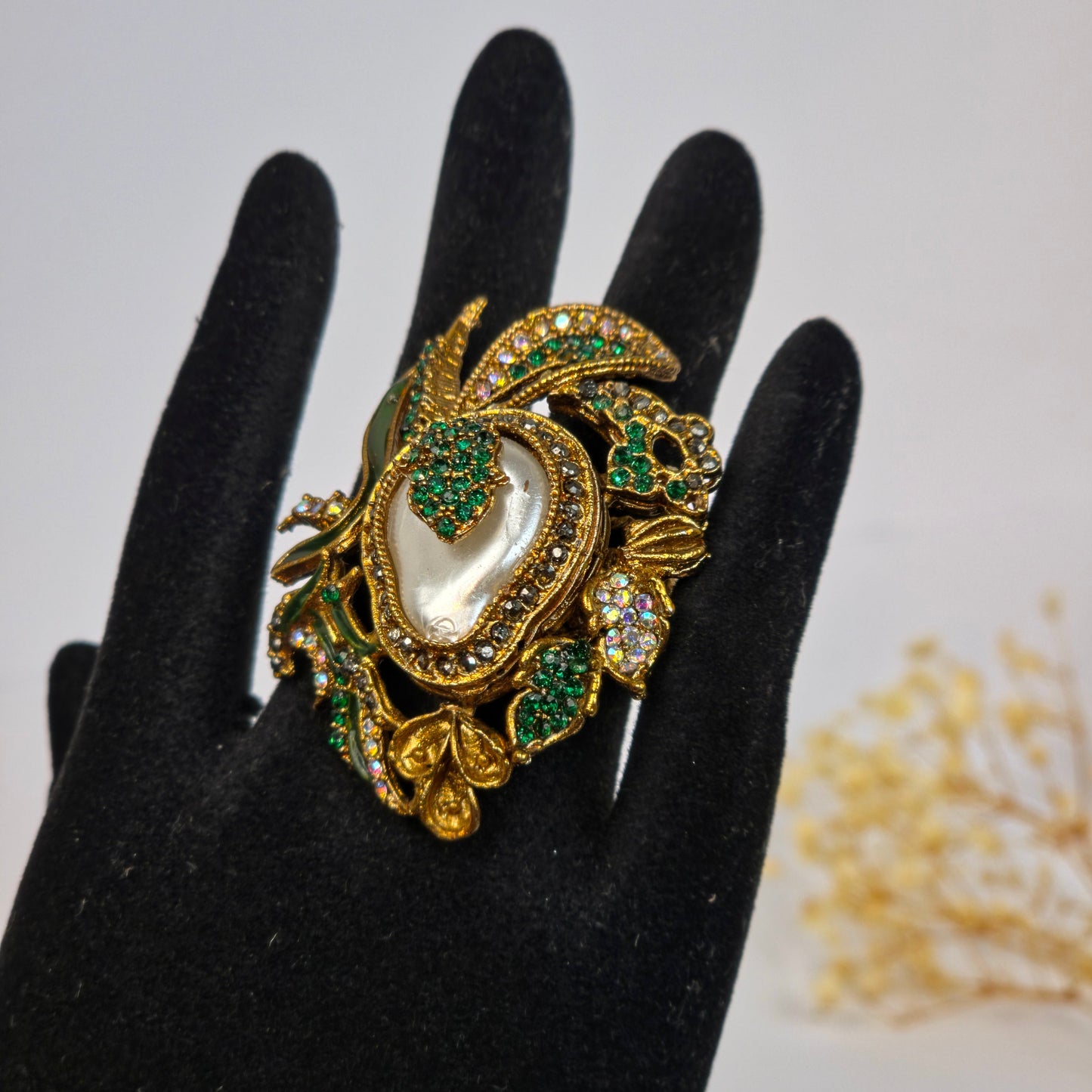 Decorative brooch with green and gold details on a black glove against a white background