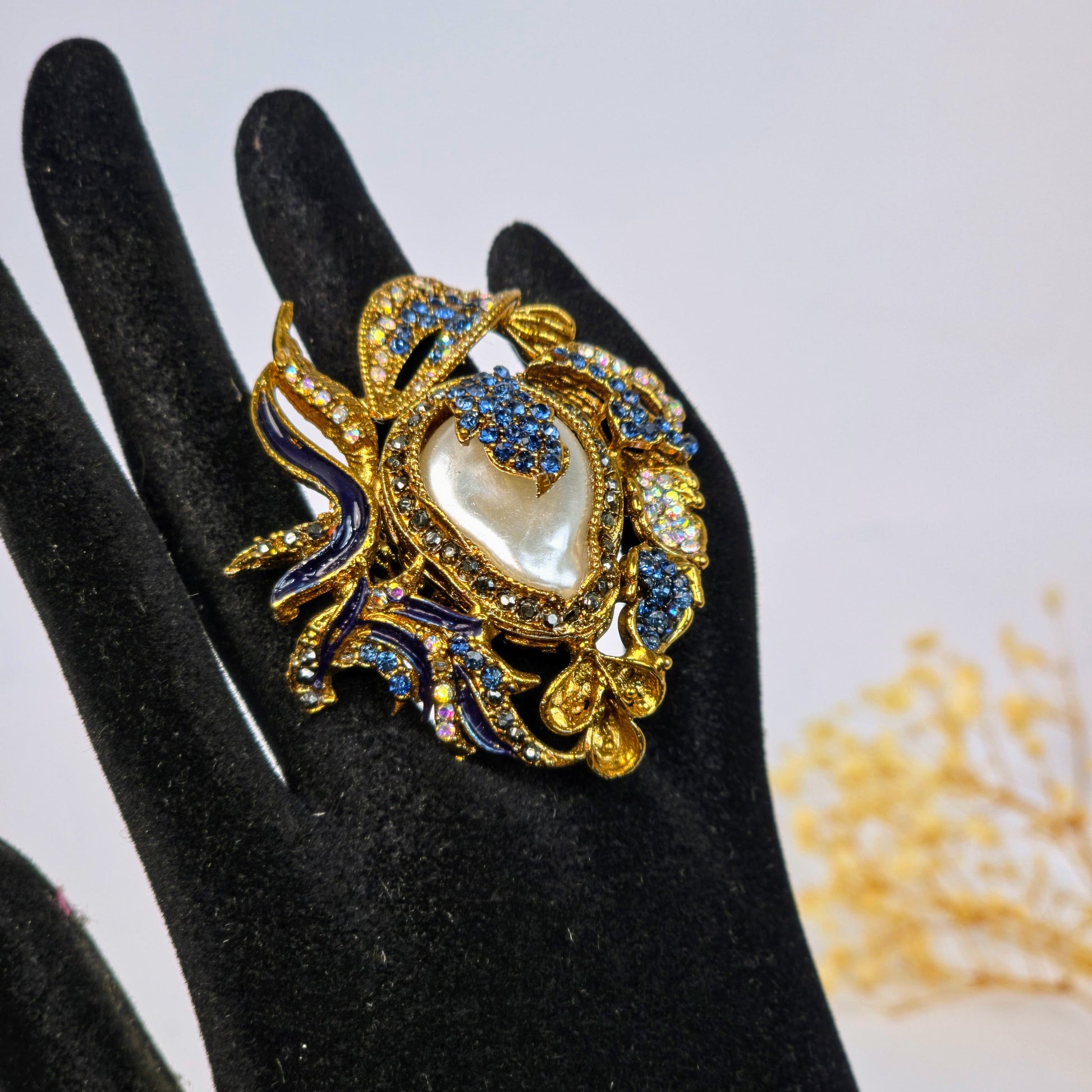 Decorative ring with pearl and gemstones on a black glove against a light background