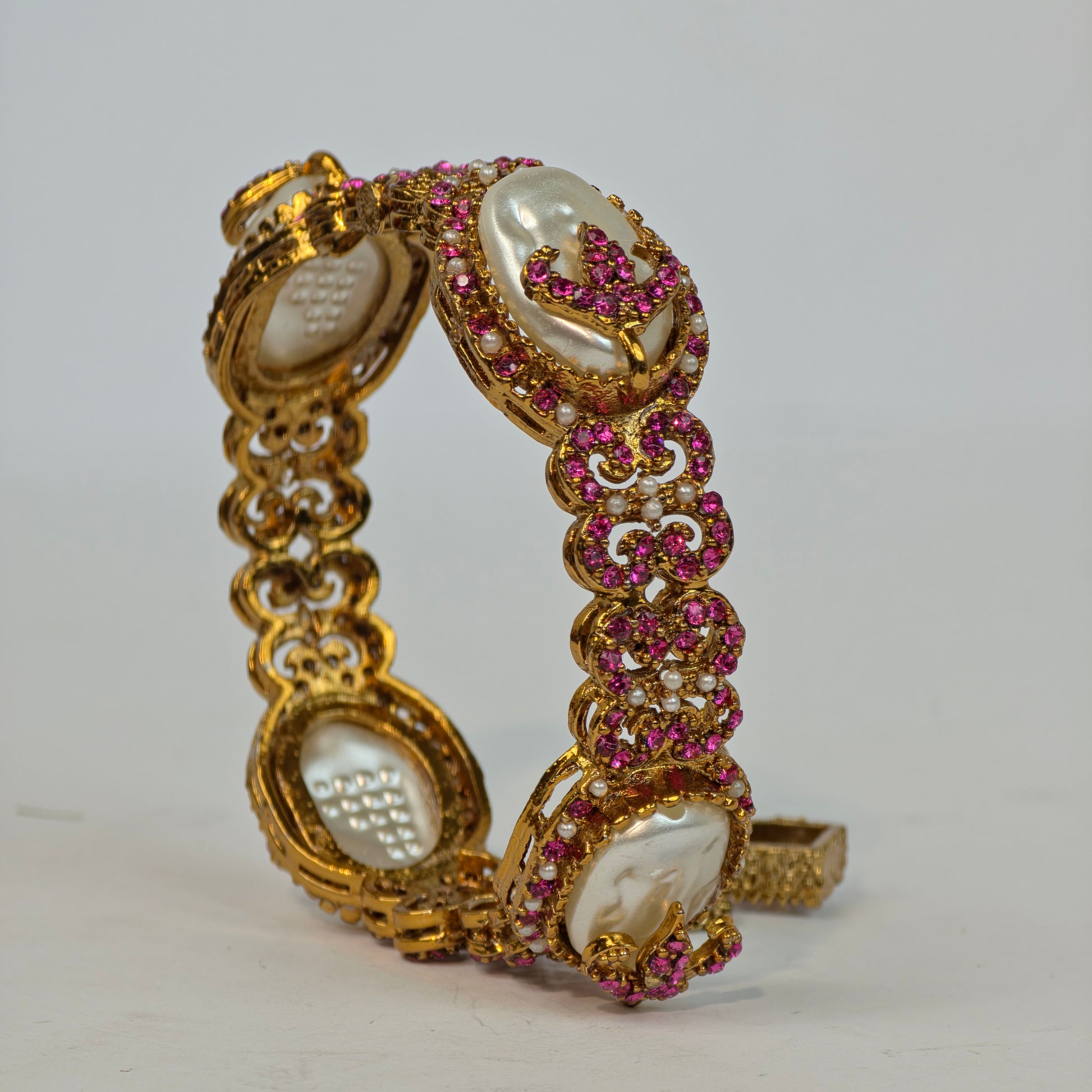 Gold bracelet with pink gemstones on a white background