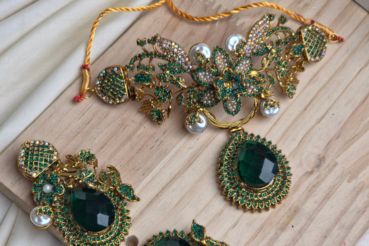 Ornate green and gold jewelry set on a wooden board with white fabric background