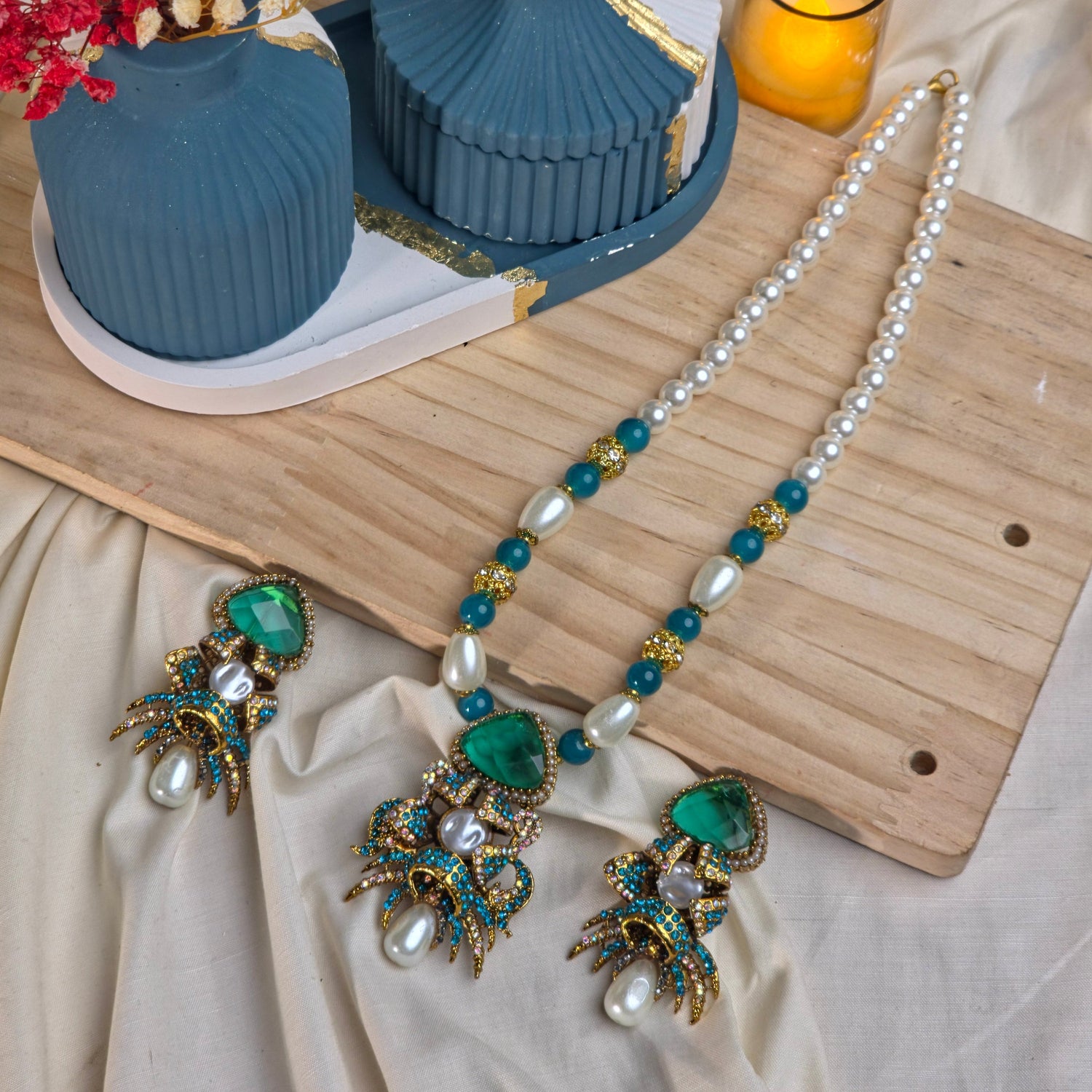 Jewelry set including a necklace and earrings on a wooden board with a candle and flowers.