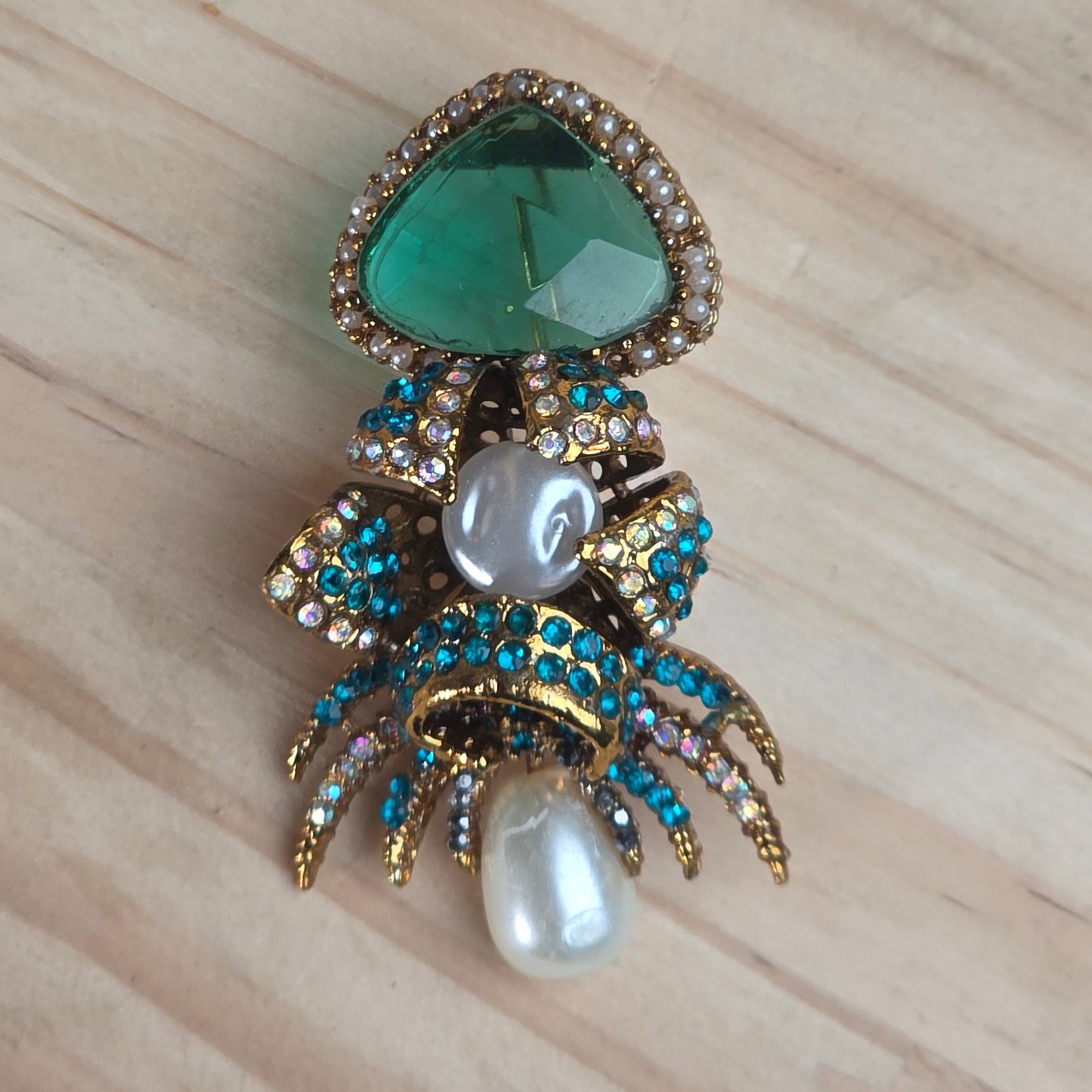Decorative brooch with green gemstone, pearls, and gold accents on a wooden surface