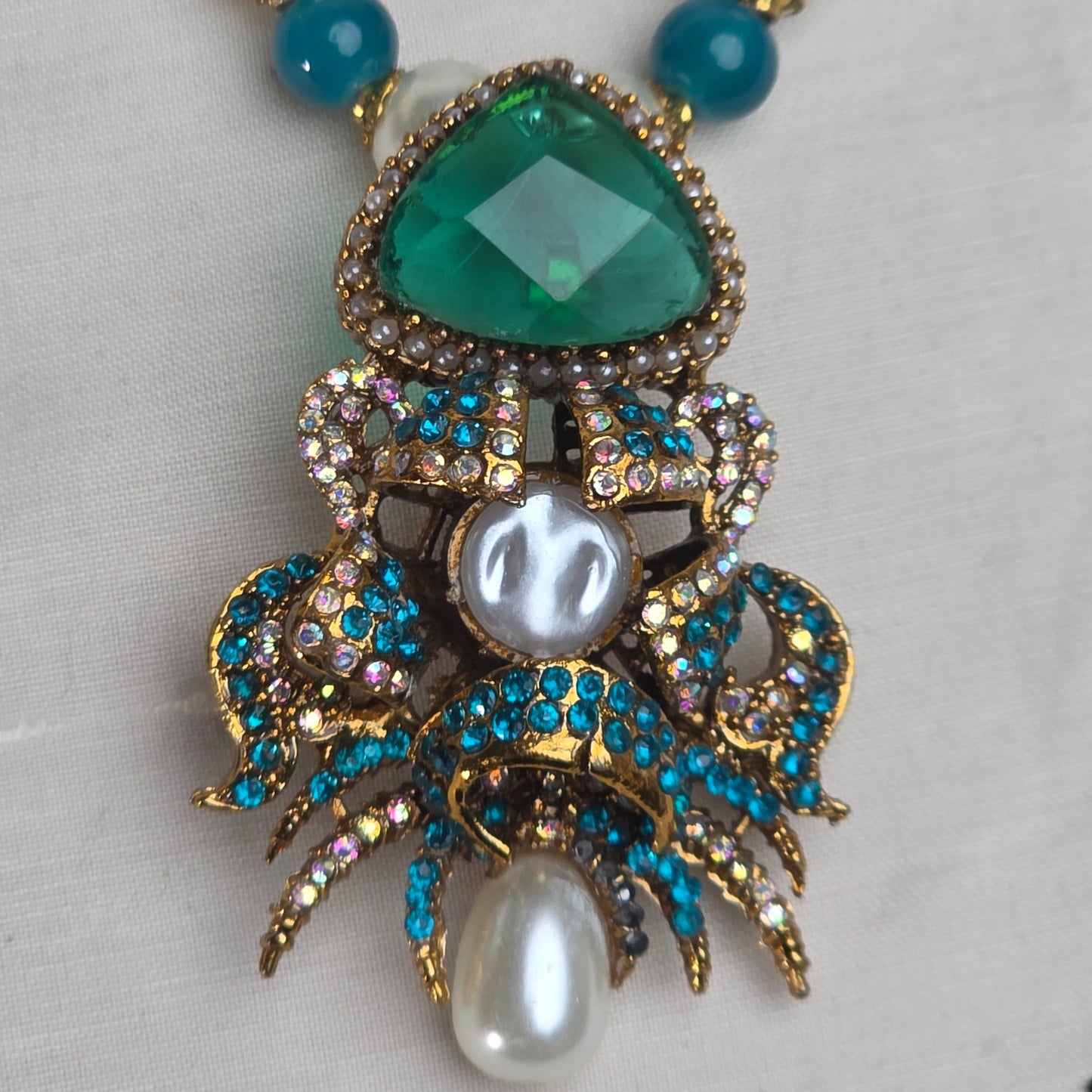 Jewelry set with green gemstone, pearls, and blue beads on a light gray background
