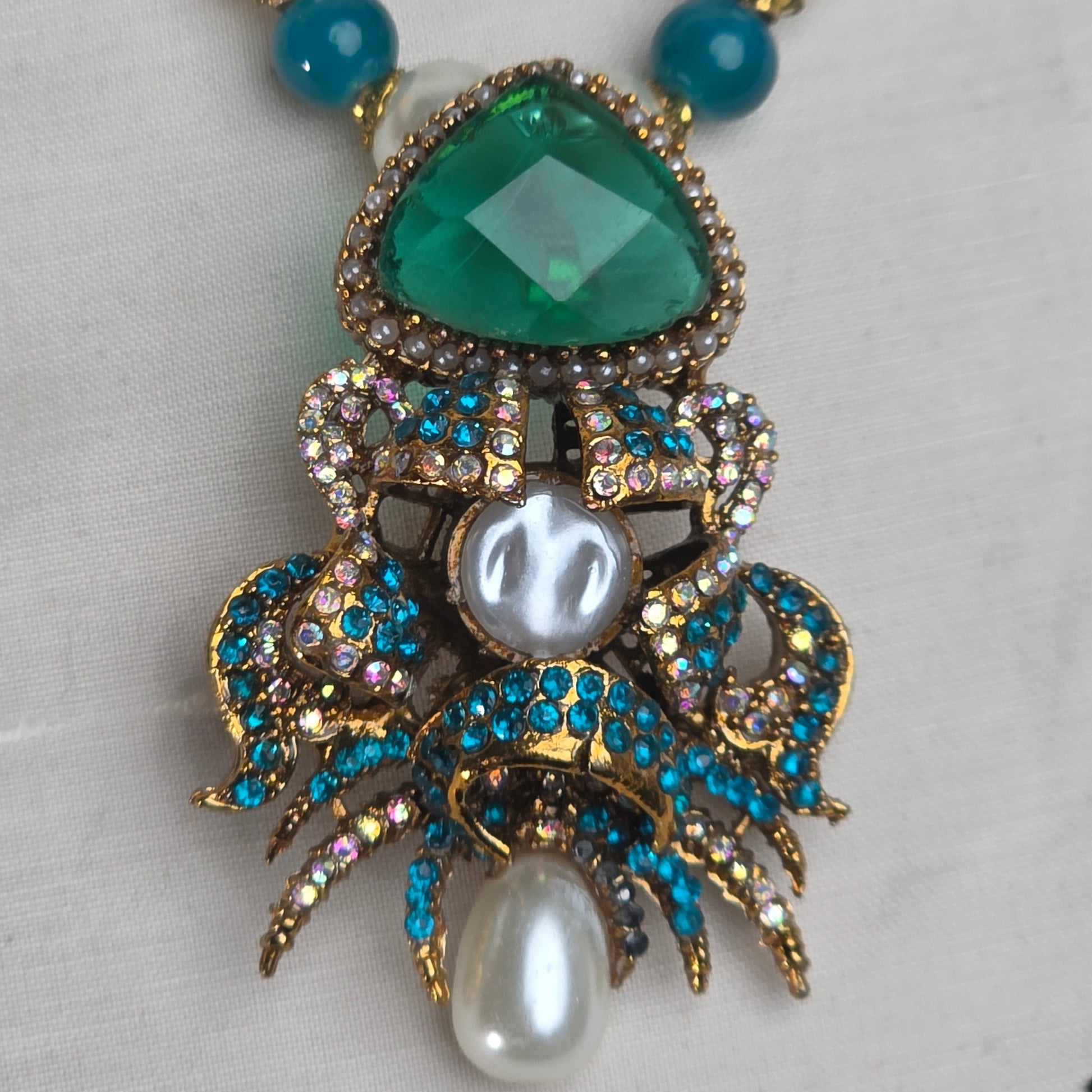 Jewelry set with green gemstone, pearls, and blue beads on a light gray background