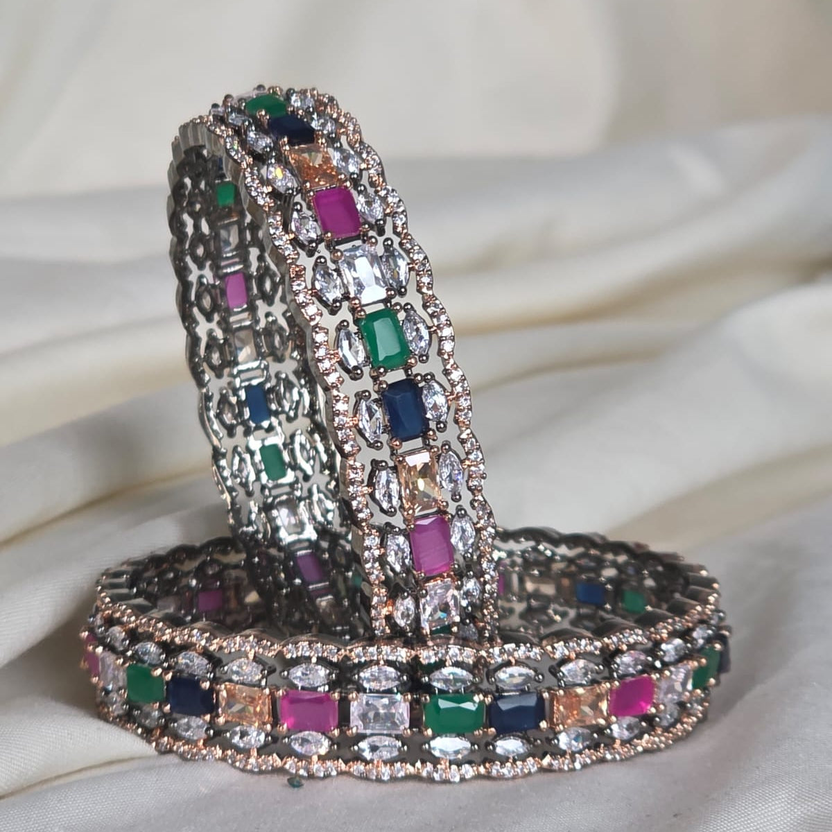 Decorative snake-shaped object with multicolored gemstones on a white fabric background