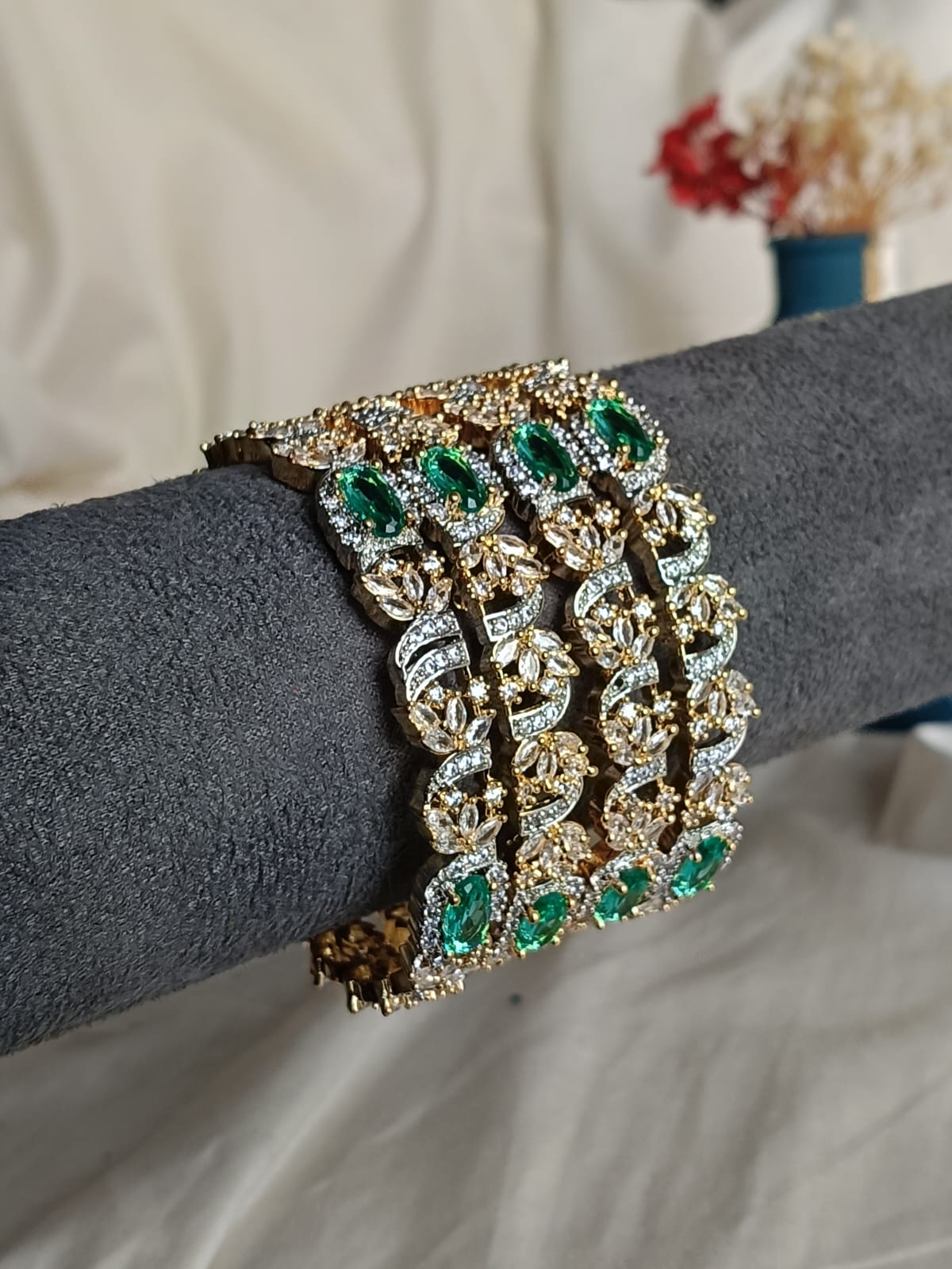 Elegant bracelet with green gemstones and gold accents on a gray arm.